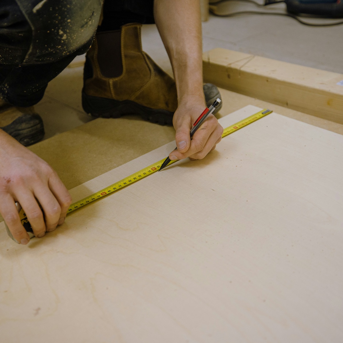 Mains mesurant et marquant un panneau de bois